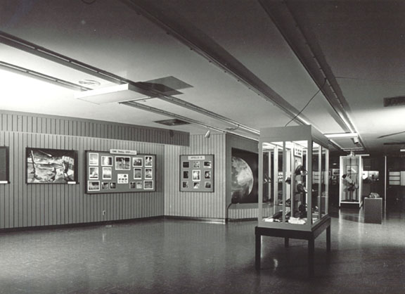 black and white photo of the original lobby design with a glass case in the foreground with a telescope and farther back a wall inset with a large Earth globe.