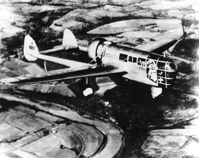 Grainy black and white photo showing a small plane flying. The front tip is all glass in a grid pattern.