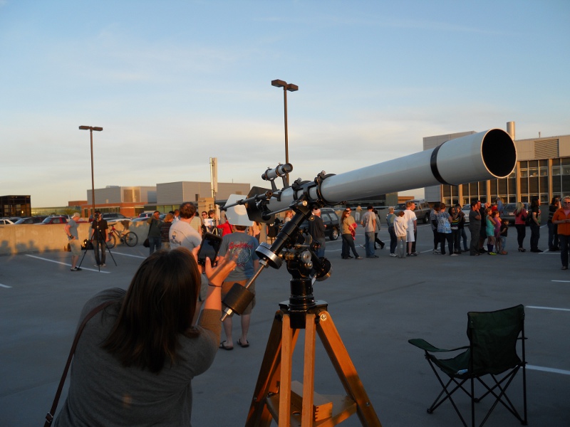 A person taking a picture through an eyepiece of a telescopes on an angled mount with a counter weight.